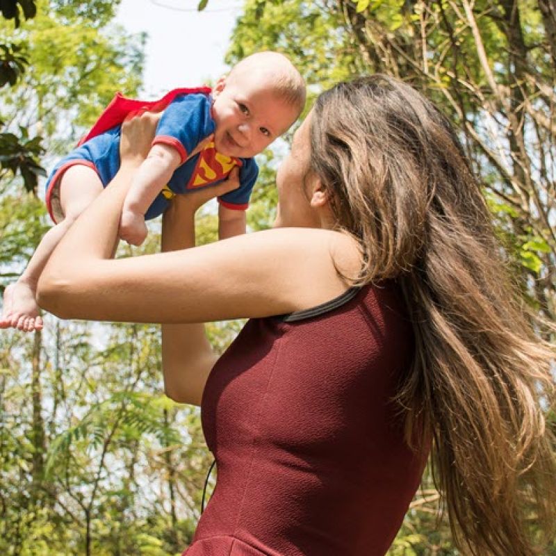 Image of a woman holding a small baby with Superman cape into the air from The Compounding Lab in Dayton, Ohio website.